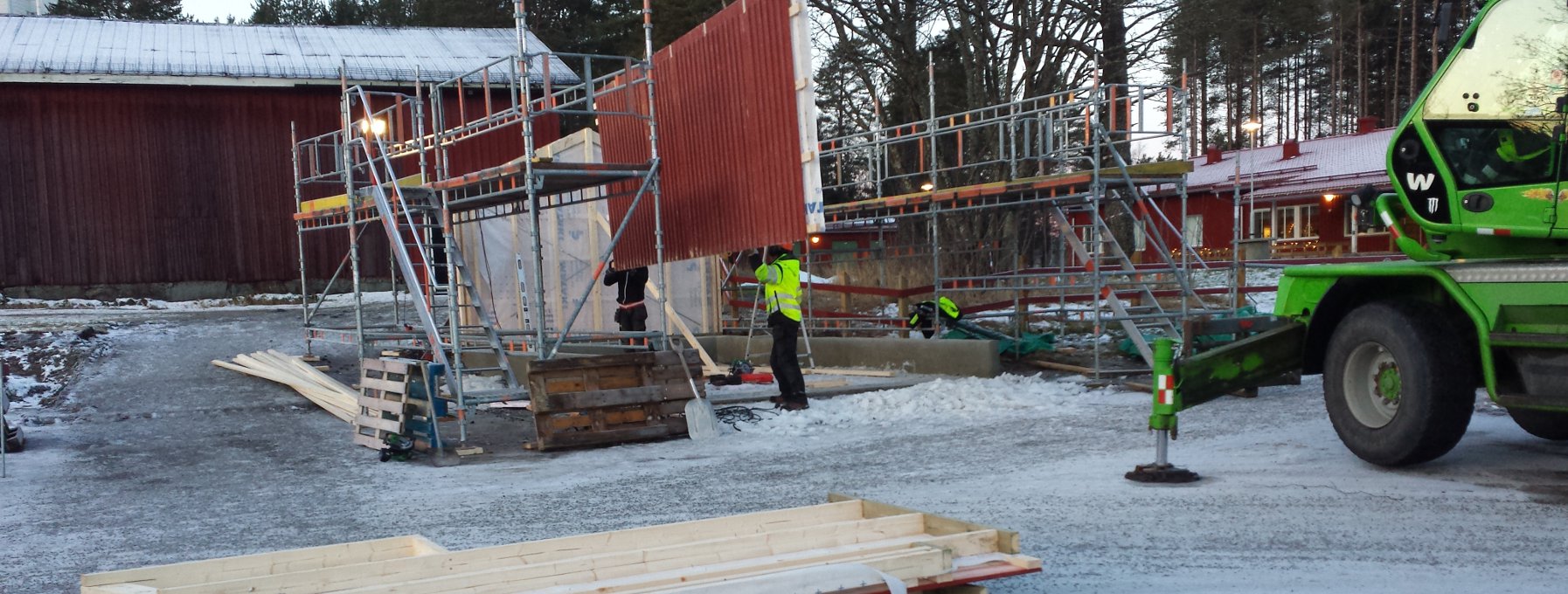 En lyftkran håller upp en vägg som byggarbetare justerar in och placerar på rätt plats