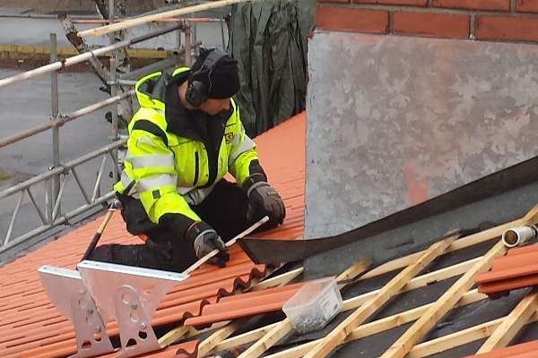 Under en pågående takrenovation tar en snickare ett mått på en tegelpanna.